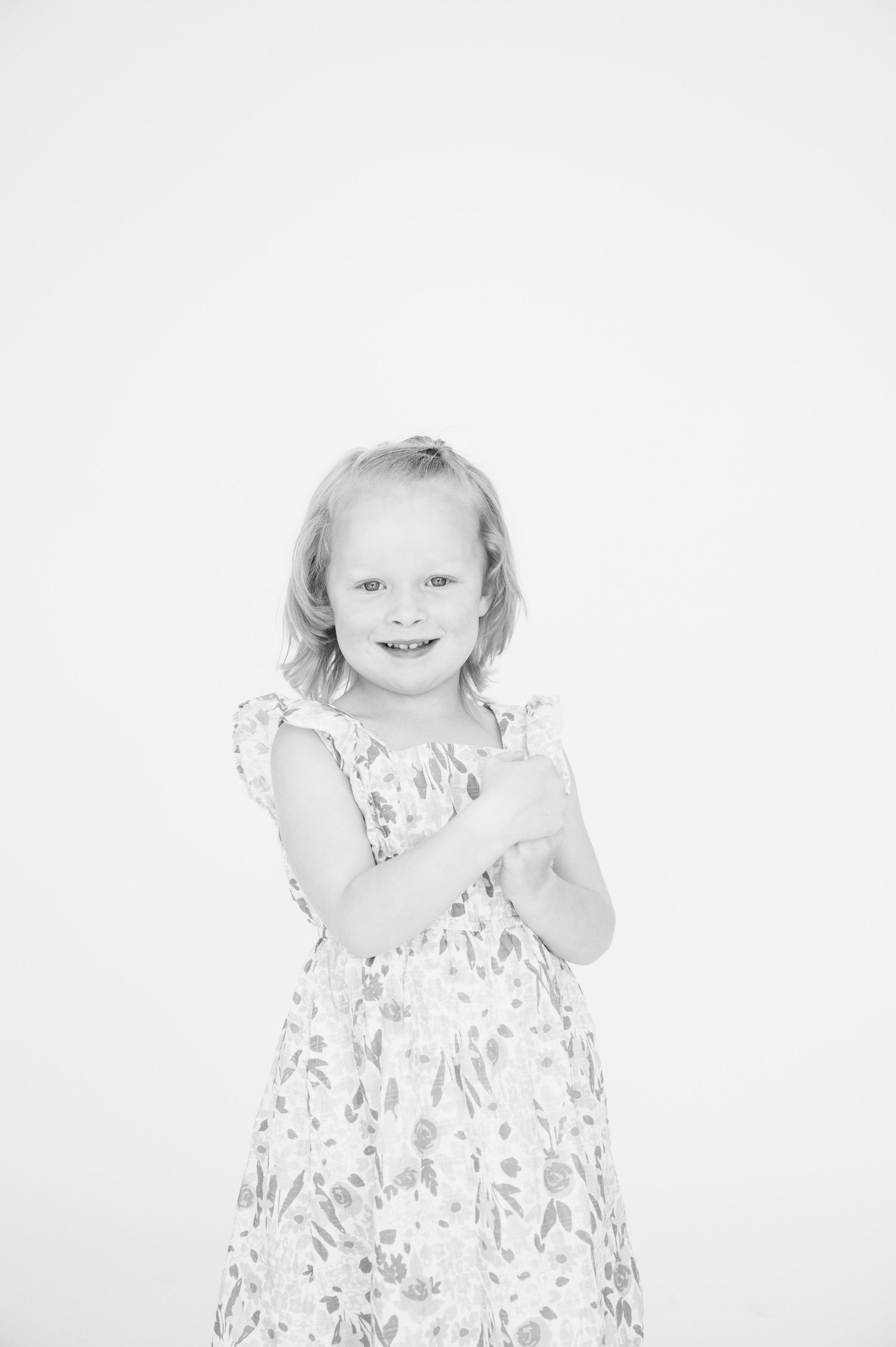 Black and white portrait of a child in a floral dress clasping hands together.