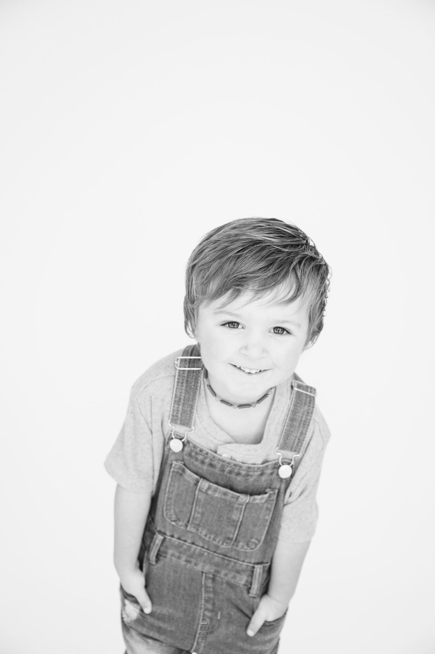 Child in denim overalls and t-shirt smiling in black and white portrait.