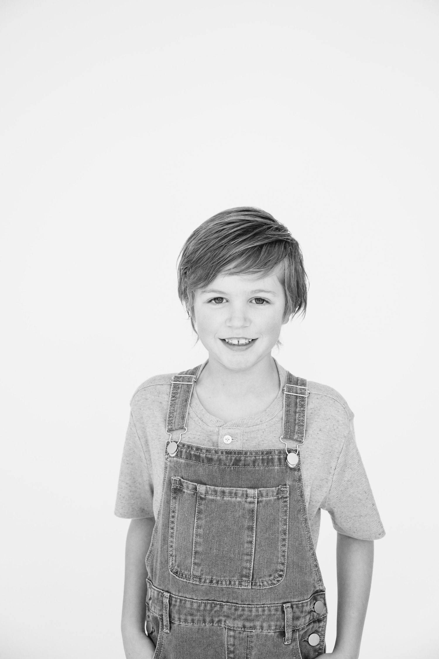 Black and white studio portrait of a child wearing denim overalls and grey t-shirt.