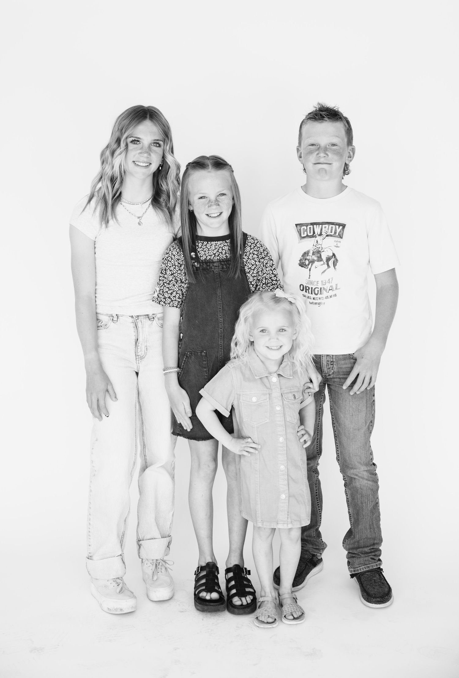 Black and white portrait of siblings in casual outfits standing together against white background.