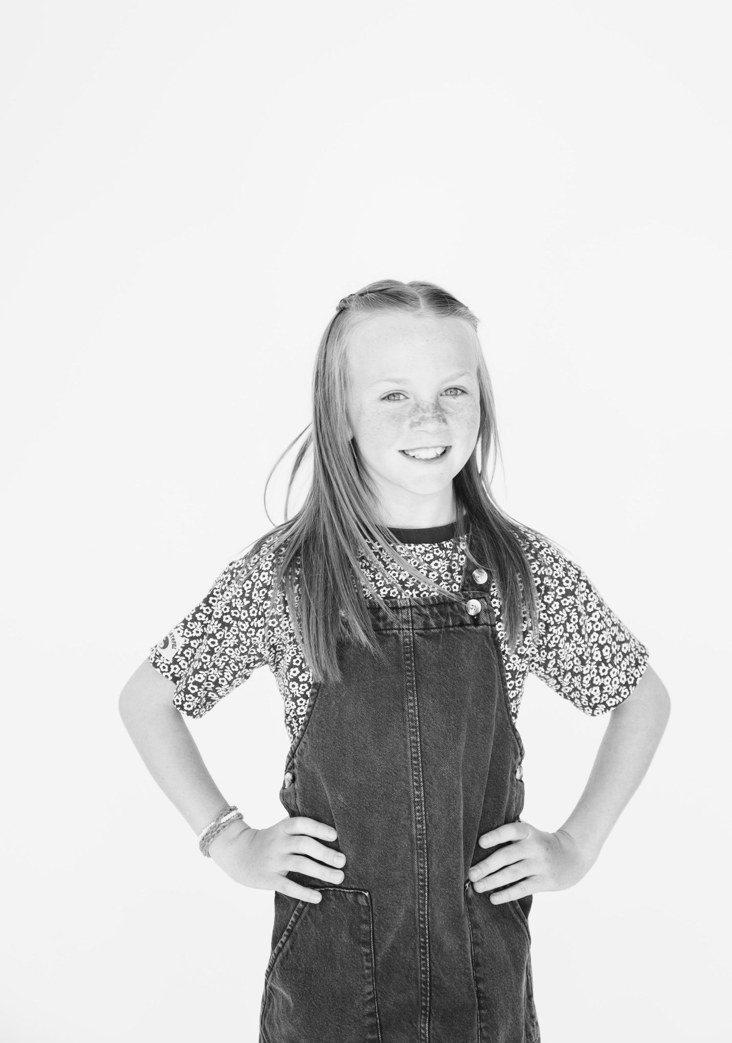 Black and white portrait of a girl in denim overalls and floral shirt striking confident pose.