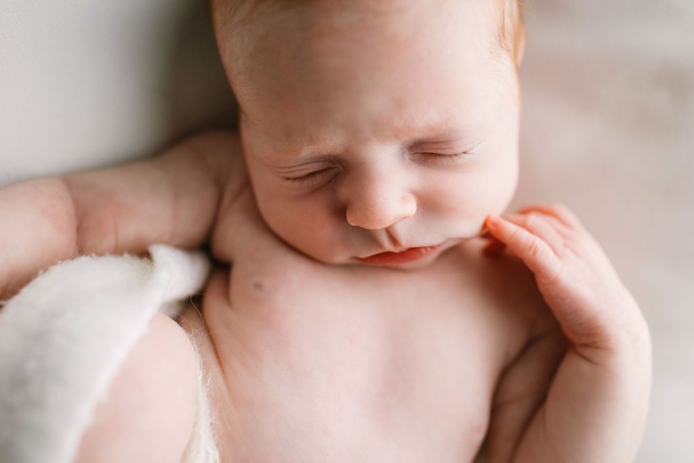 Peaceful sleeping baby wrapped in soft white blanket during newborn photography session.