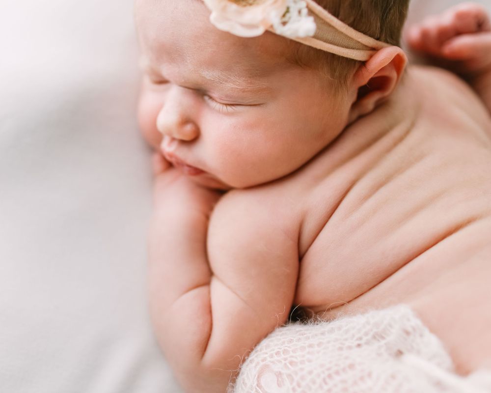 Peaceful sleeping newborn baby photographed by Jillian Kennedy on soft white blanket.