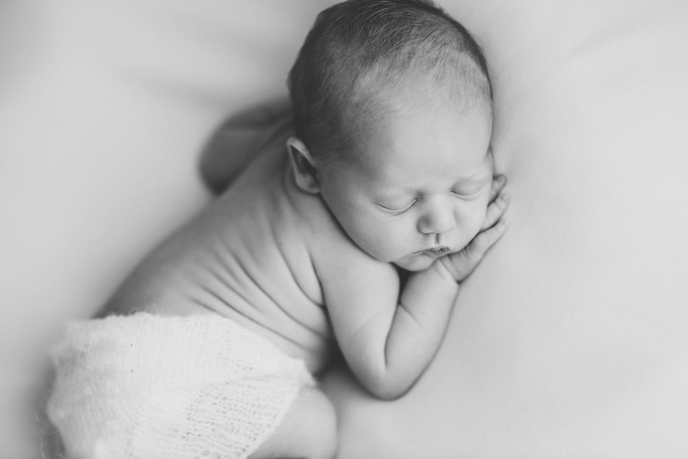 A sleeping newborn baby dressed in white in a black and white portrait done in Jillian Kennedy's Halifax studio