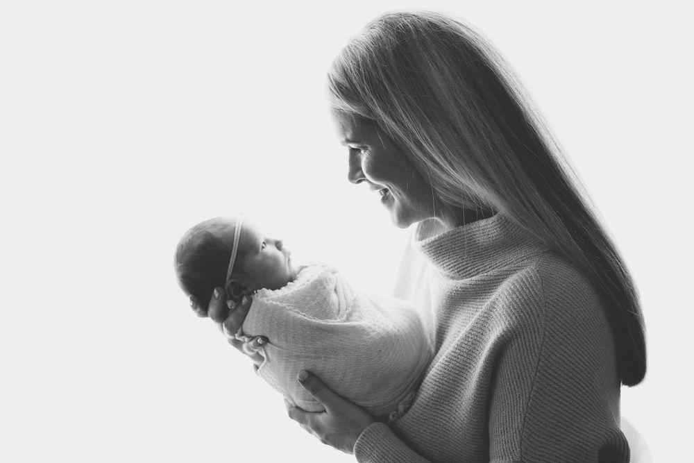 A tender black and white portrait of a mother cradling her newborn baby in gentle window light taken by Jillian Kennedy Photography