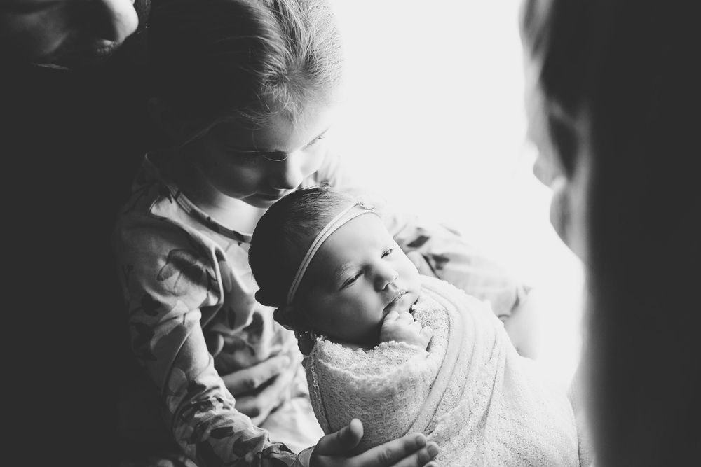 A tender black and white photo of a swaddled newborn baby being cradled.