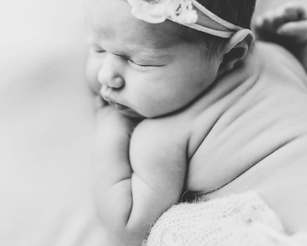 A sleeping newborn baby wearing a delicate white headband rests peacefully in black and white photography.