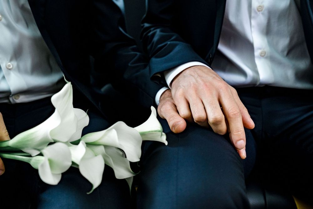 Close-up of hands resting on a lap next to white calla lilies on formal attire.