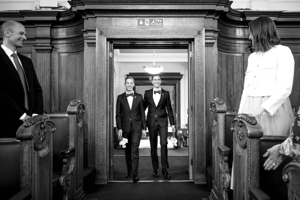 Black and white photo of a couple walking through an elegant wooden doorway in formal attire.