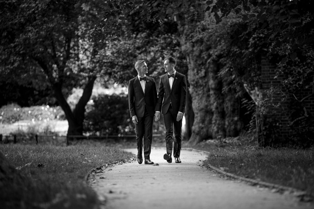 A black and white photo of two people walking together on a tree-lined path.