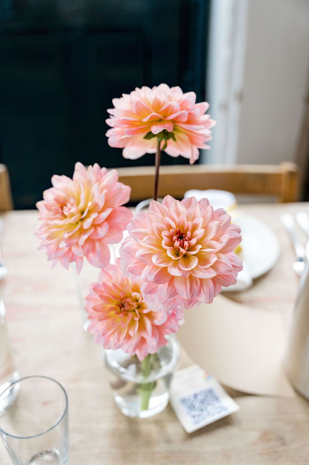 Pink and peach dahlia flowers arranged in a clear glass vase on a wooden table.