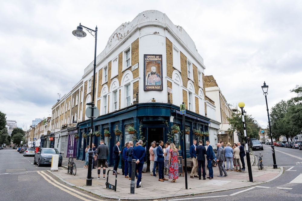 A busy corner pub building with vintage architecture and people gathering outside on a London street.