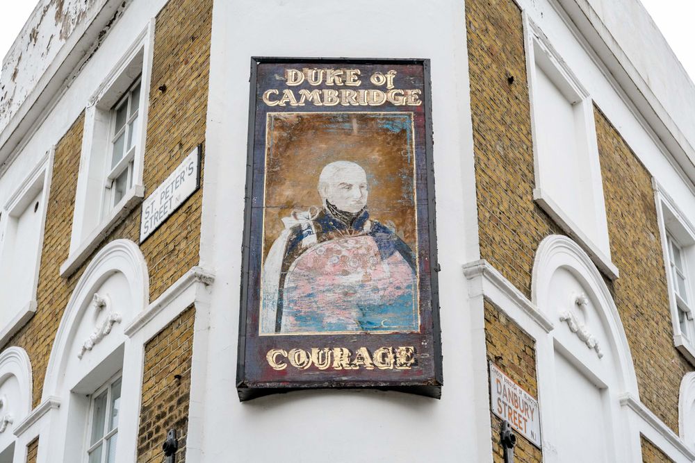 Vintage pub sign for Duke of Cambridge mounted on corner of brick building.