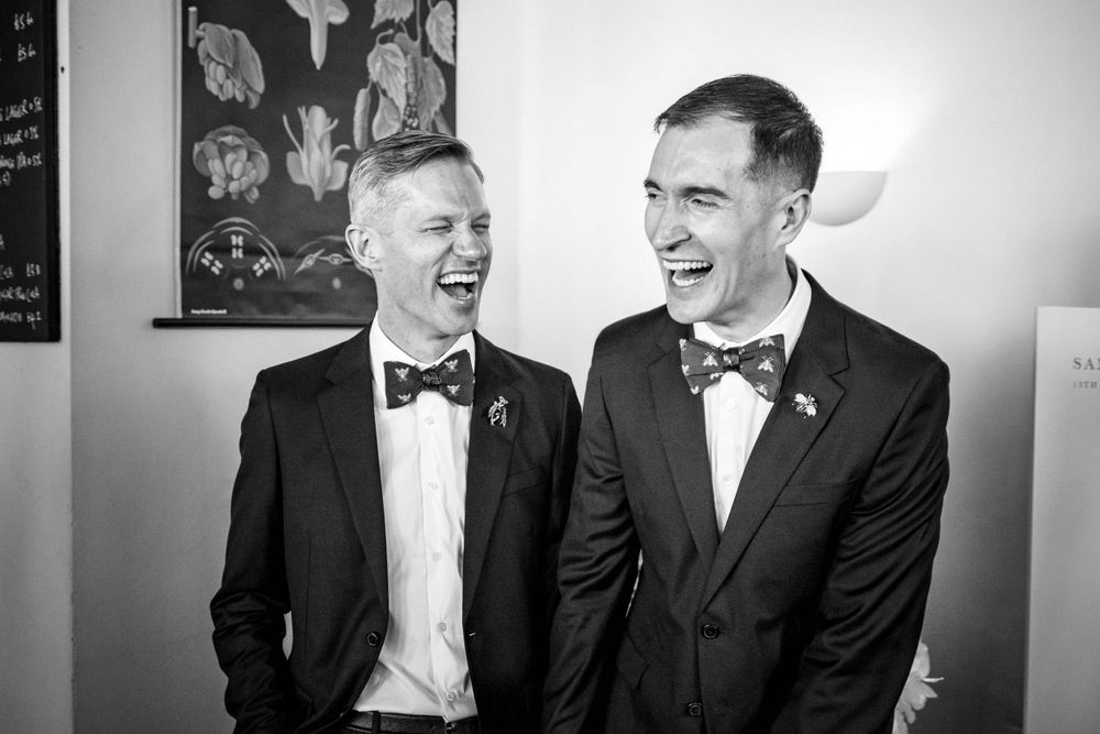 Two people in bow ties and formal suits share a candid laughing moment.