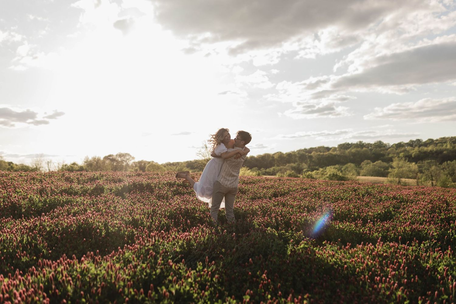 A couple embracing in a field of flowers during golden hour sunset.
