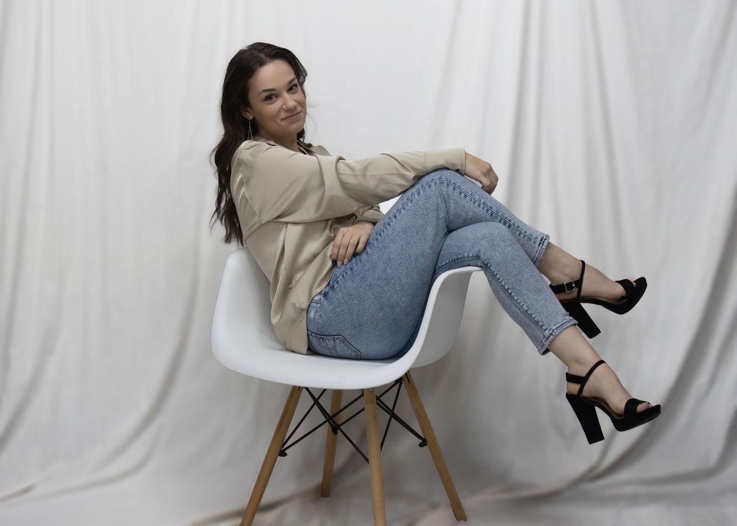 Portrait of woman lounging in modern white Eames chair against white backdrop.
