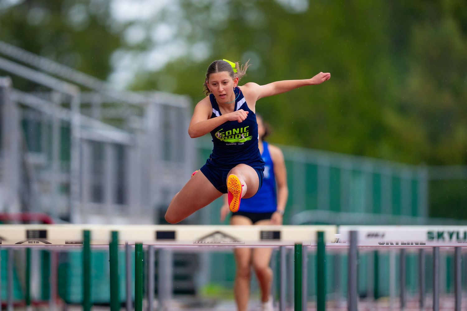 A women's track & field participant is in mid-air going over a hurdle.