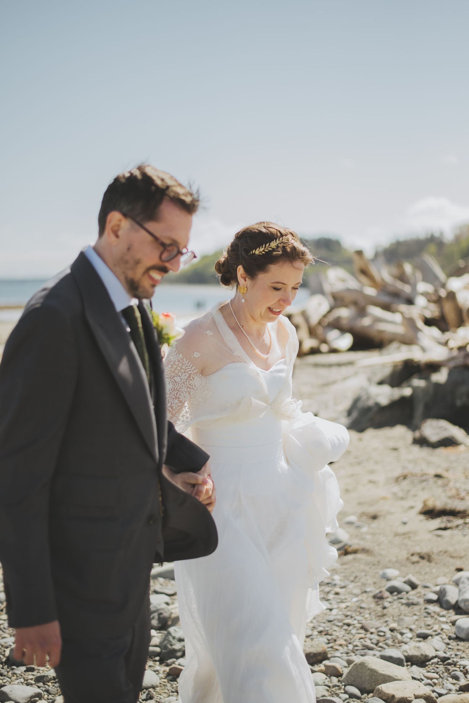 A couple walk together on a rocky beach, the bride's dress flowing in the wind.