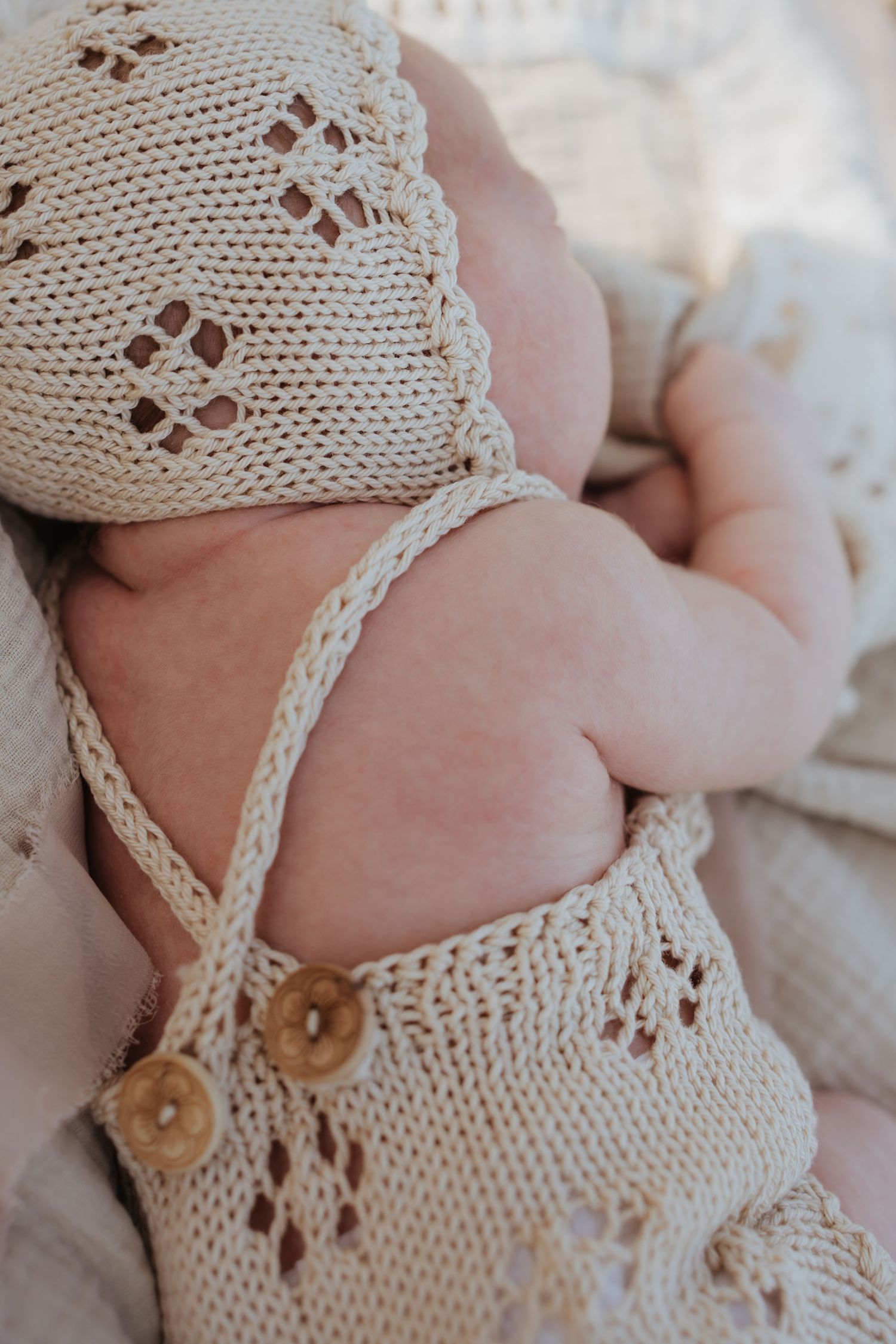 Close-up of baby feet wearing delicate cream knitted booties with lace details and wooden buttons.