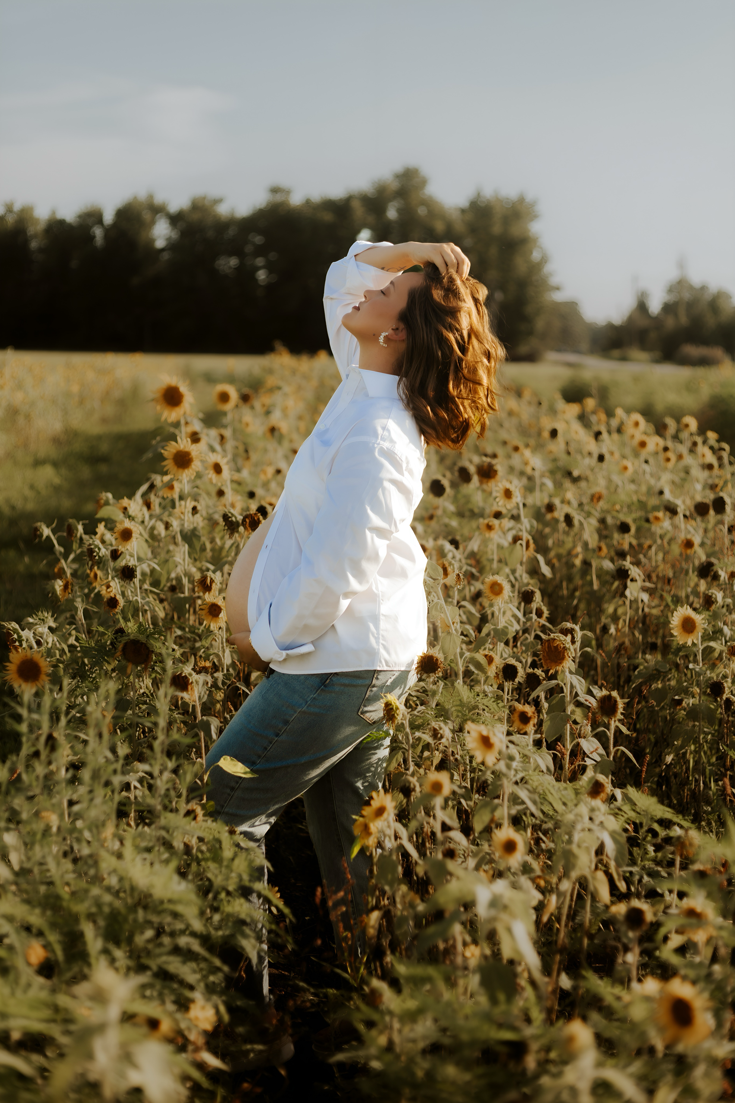 Ethereal maternity photography in sunflower field at golden hour.