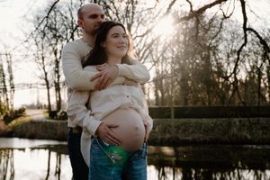Maternity photo session at sunset by a serene lake with bare winter trees.