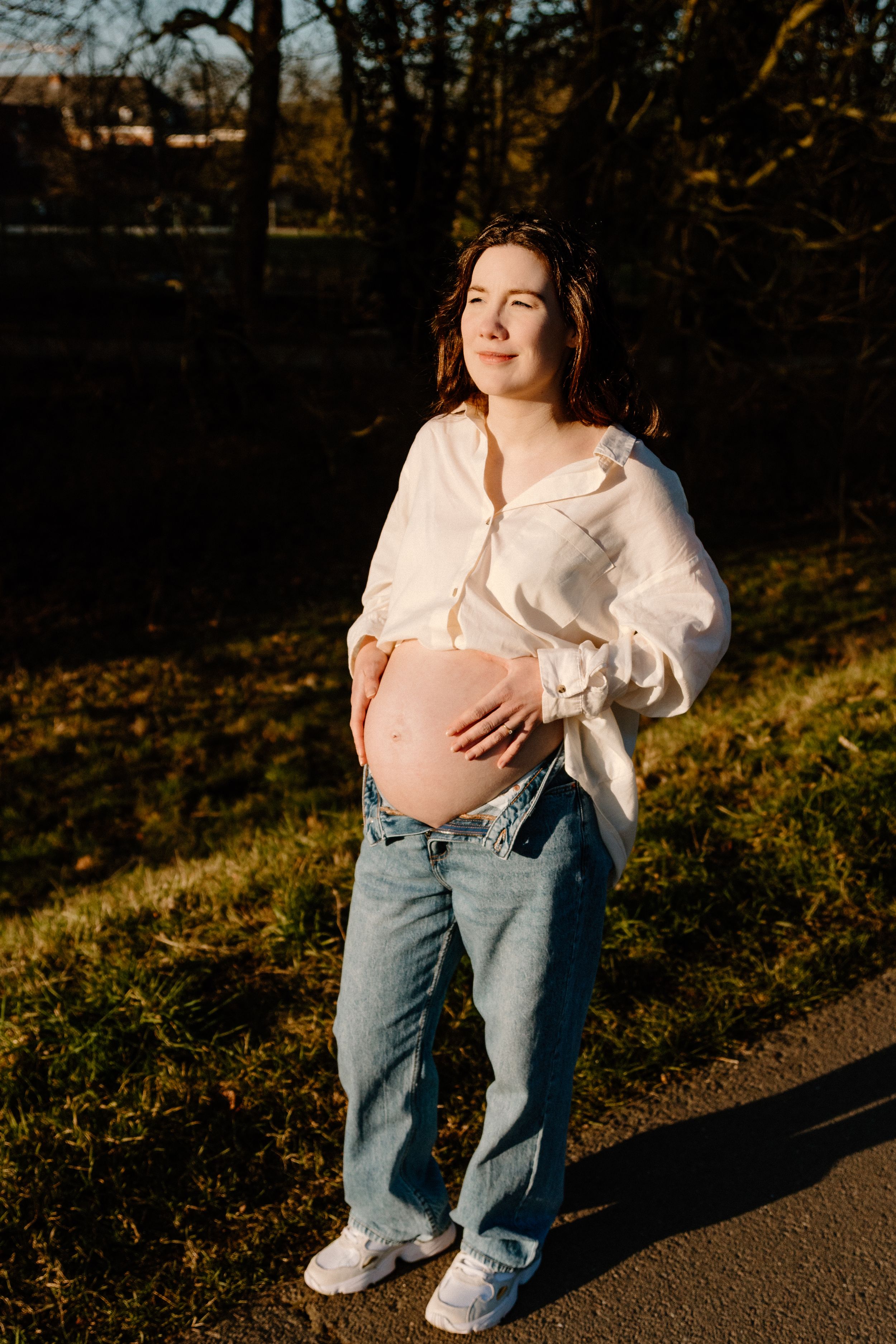 Maternity portraits in warm sunlight featuring white top and classic blue jeans.