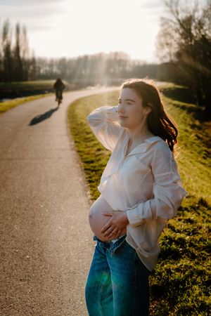 Person in white shirt and jeans poses against golden sunlight on a rural path.