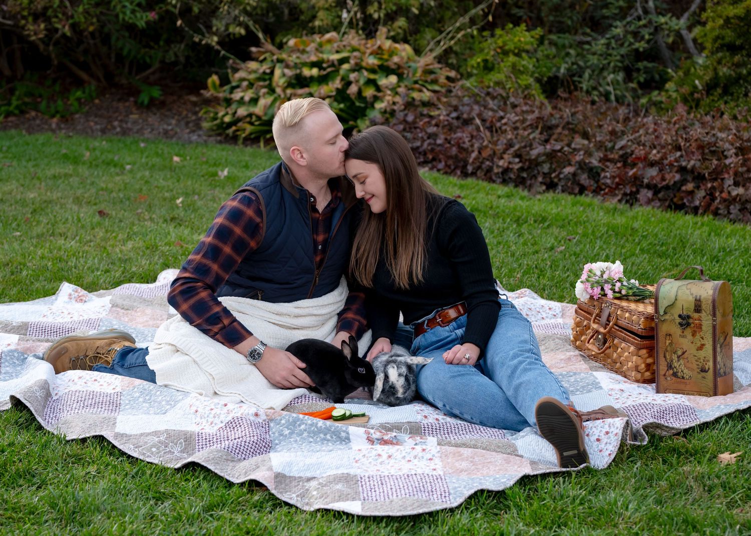 A couple sitting in a picnic setting with their two bunnies while husband kisses wives forehead. Wrightstown NJ Family Photographer