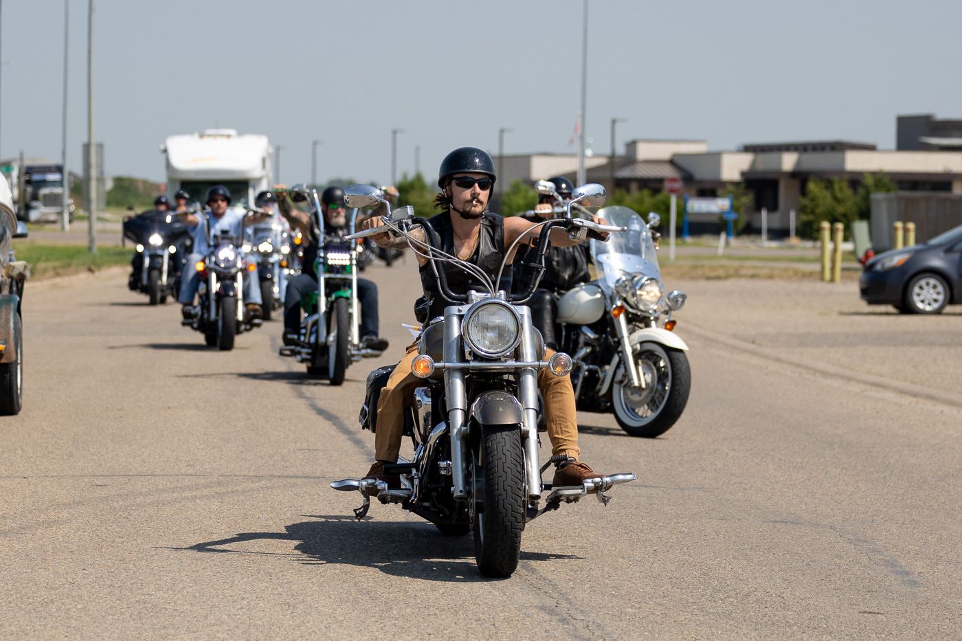Group of motorcyclists riding in formation on a road, led by rider in black clothing.