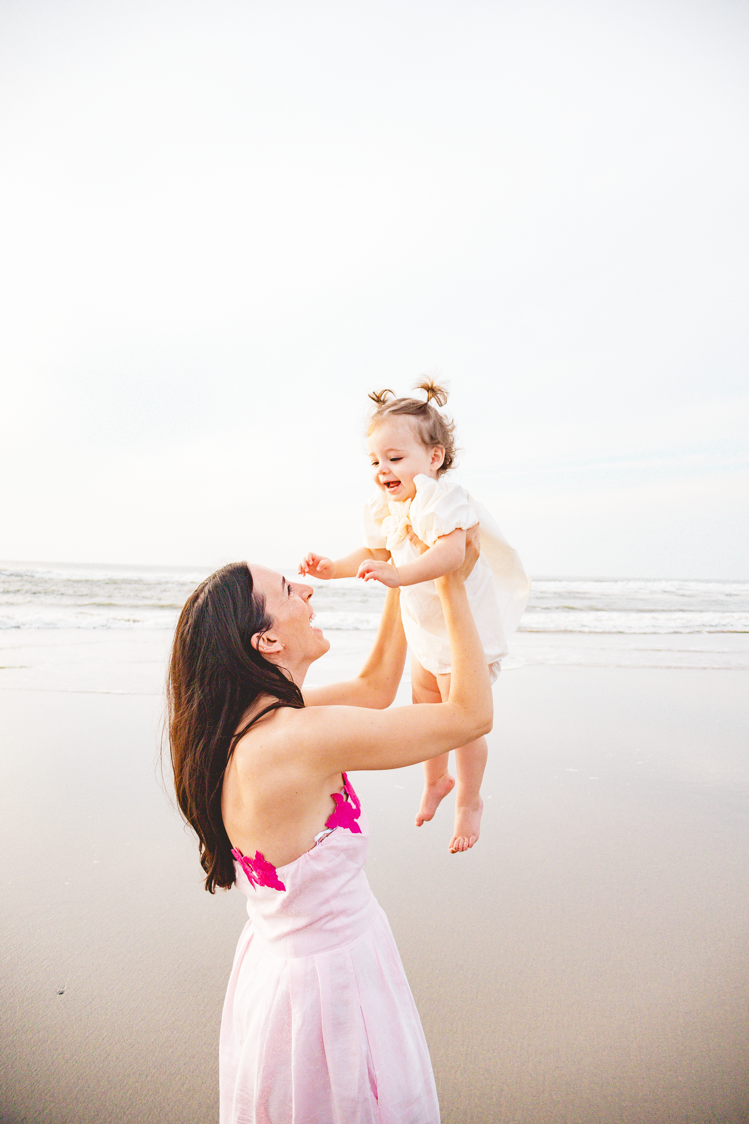 Mother and baby playing together on a sunny beach in pink attire.
