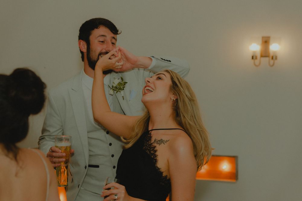 A laughing couple in festive attire shares a playful moment at a party, with the woman touching the man's face.