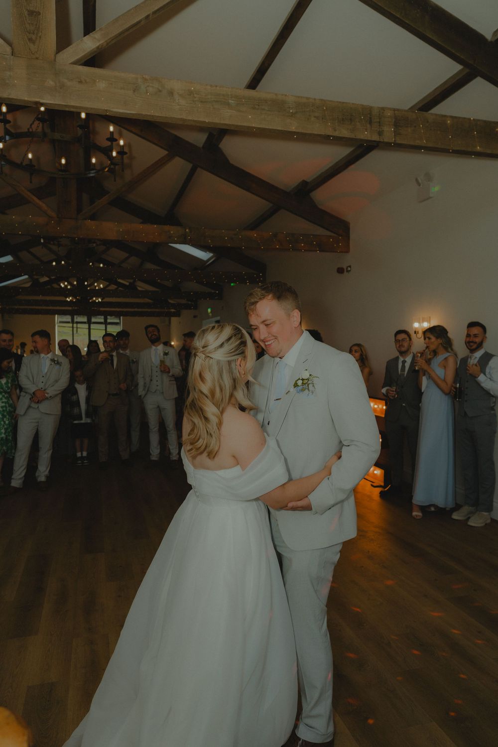 Bride and groom sharing their first dance in a rustic barn wedding venue with exposed wooden beams and warm lighting.