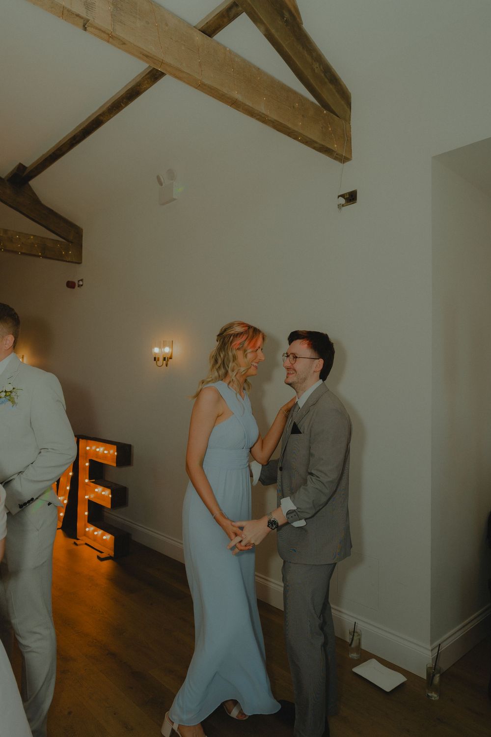 Couple sharing a tender moment at a wedding reception in a rustic barn venue with illuminated letter decorations.