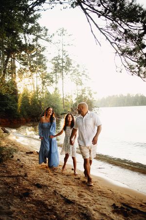 Family holding hands walking on the beach at Clarks Hill Lake.  Mother and daughter are looking lovingly at the father.
