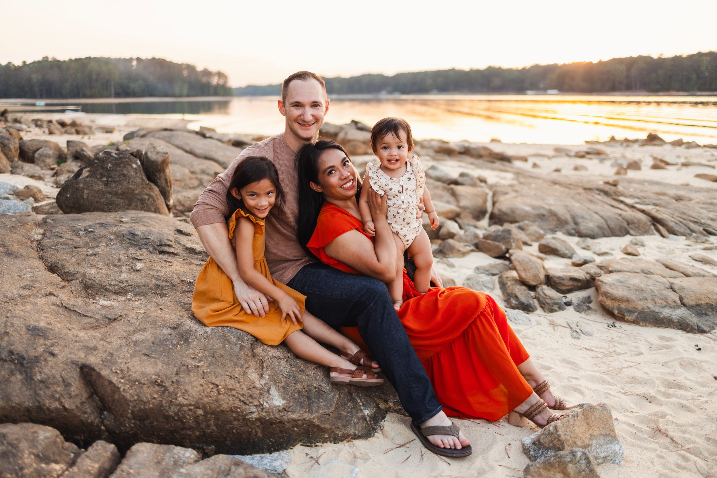 Family group sitting together on large rocks by lake during golden hour.