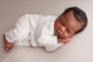 Peaceful sleeping newborn baby wearing white outfit lies on soft textured fabric.