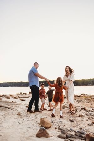 Family dancing together on rocky beach at sunset with lake and trees in background.