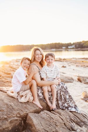 Family enjoying sunset together while sitting on rocky beach shore.
