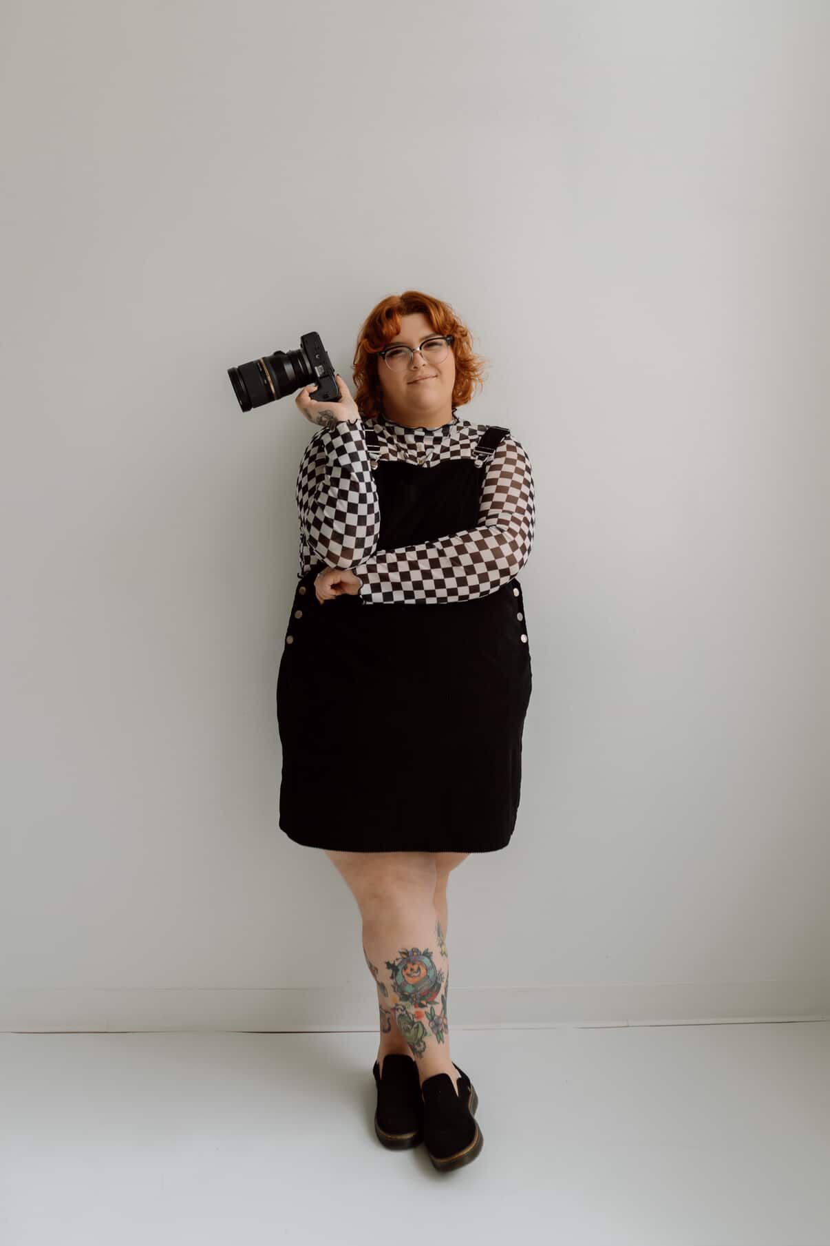 Person in floral dress and glasses poses playfully against warm glowing lights in indoor setting.