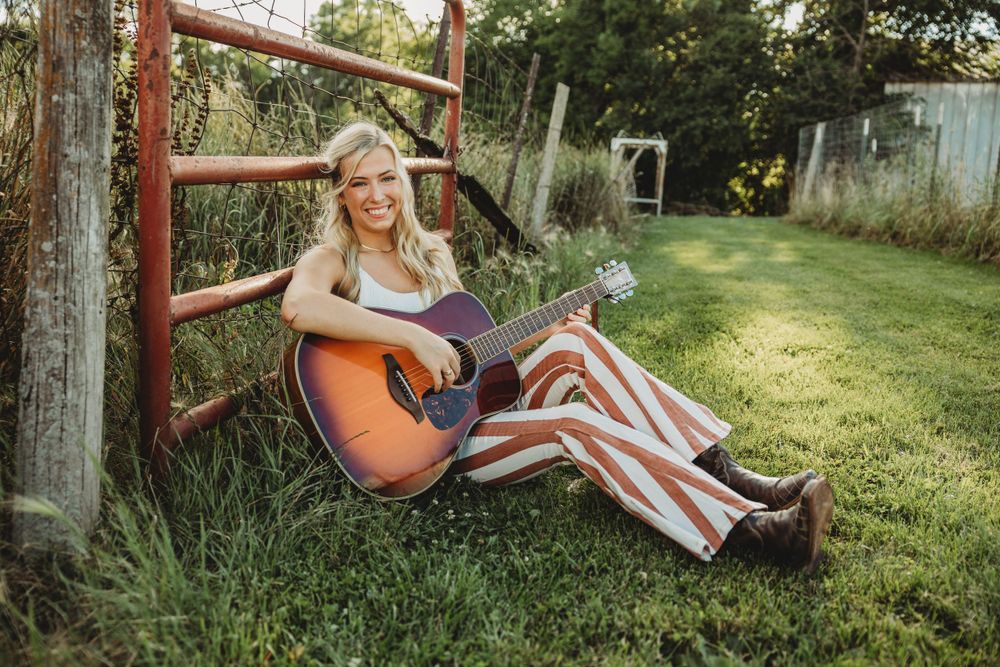Person playing guitar while sitting on wooden steps near a rustic barn.