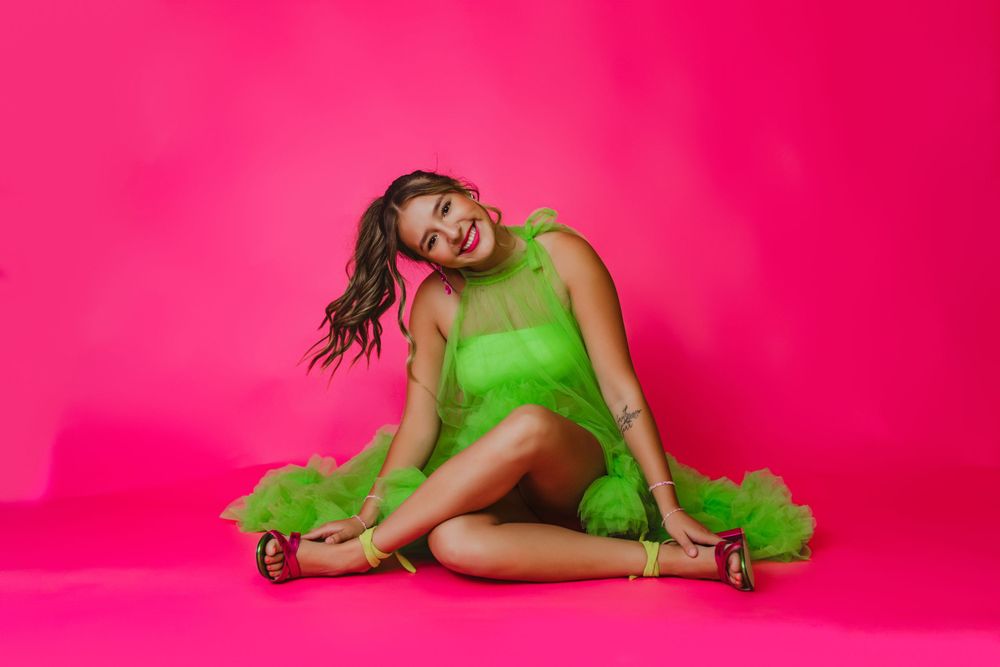 Fashion model poses on vibrant pink backdrop wearing green tulle outfit.