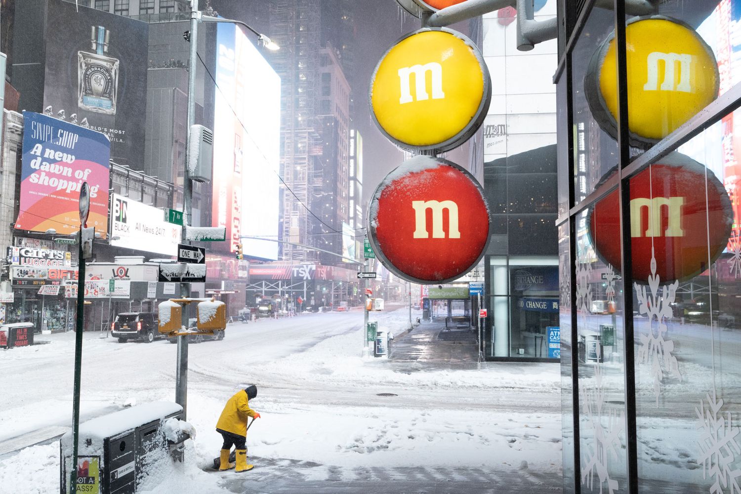 Yellow and red M&M store signs in Times Square during a snowstorm.