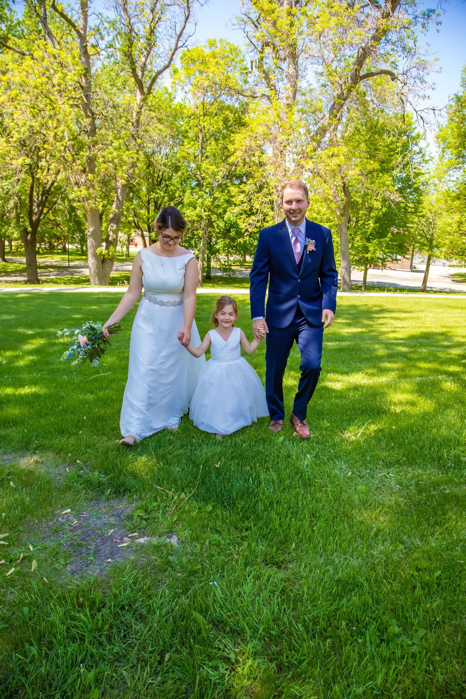 Wedding party poses on green lawn with trees in background during outdoor ceremony.