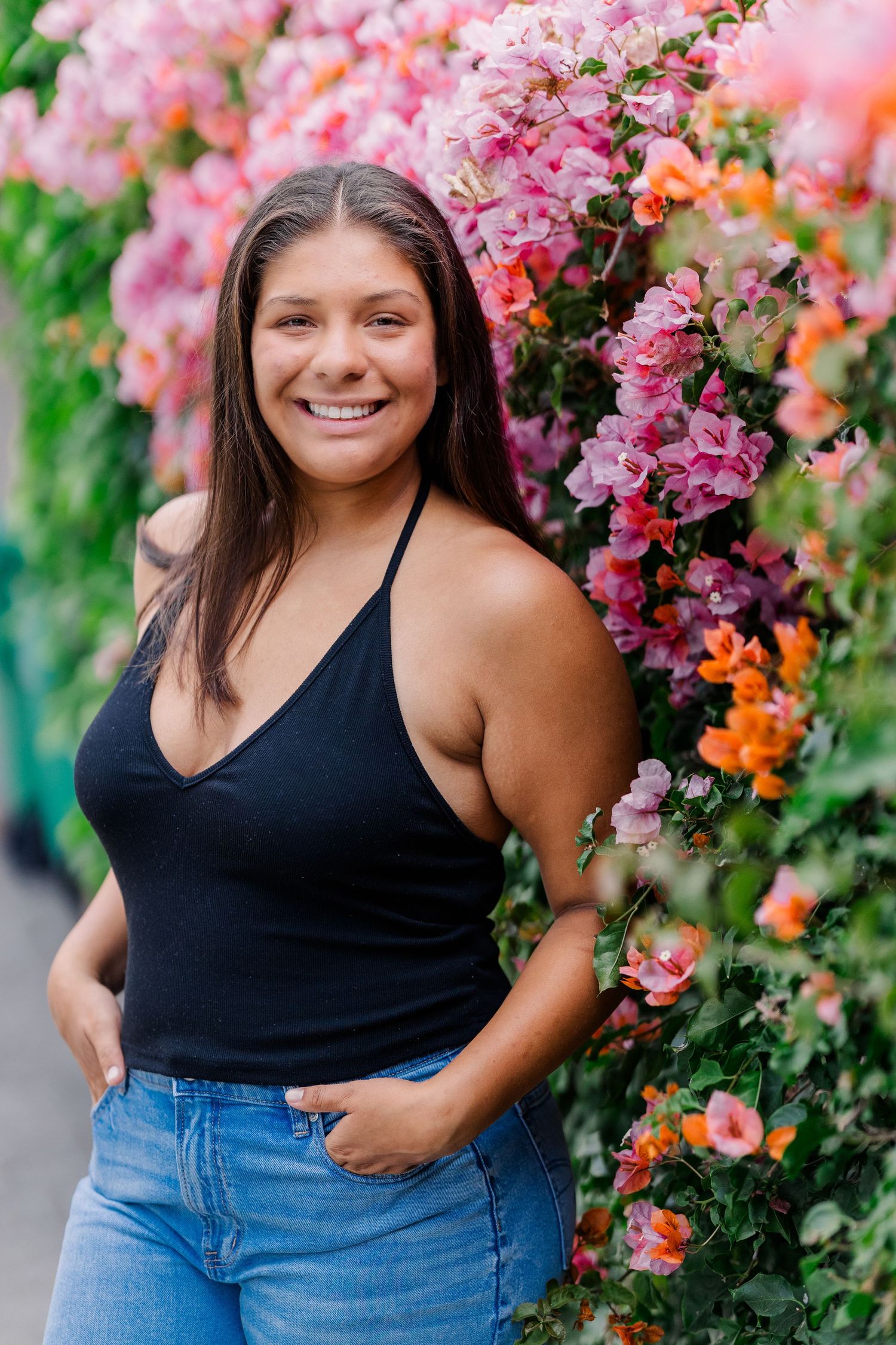 Person in black tank top and jeans poses beside vibrant pink bougainvillea flowers.