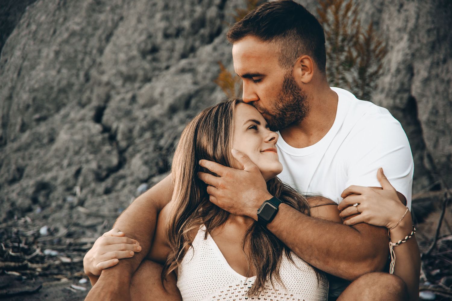 Man kissing woman's forehead while sitting on the beach