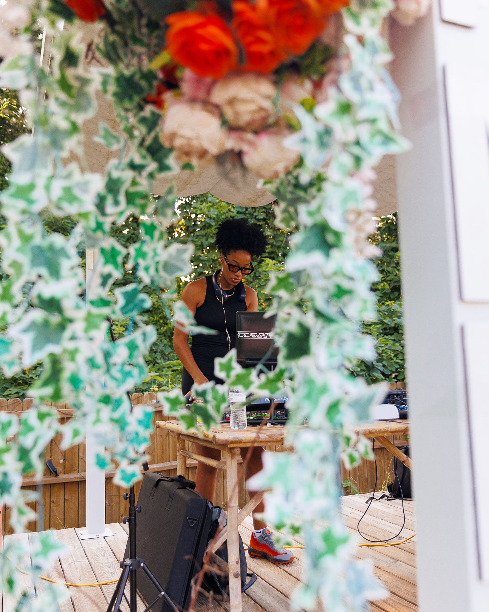Artistic shot of DJ setup framed by floral decorations and greenery.