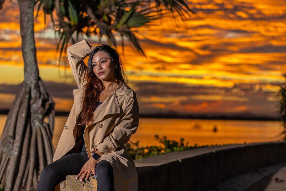 Dramatic orange sunset sky provides backdrop for silhouette posing by the waterfront.