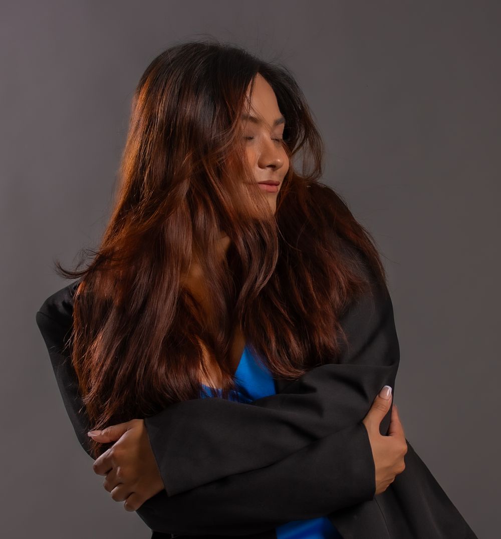 Artistic portrait showing movement of long hair while wearing black jacket and blue top.