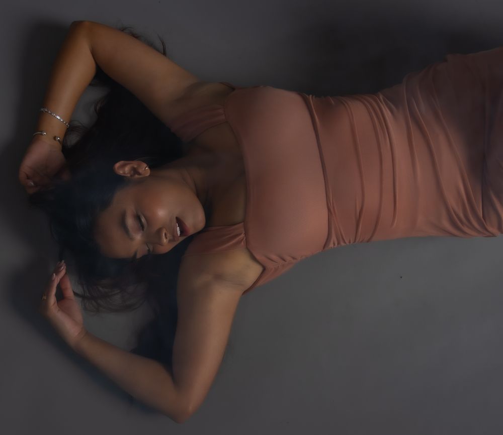 A series of artistic dark moody photographs showing a person in salmon-colored clothing reclining against a black background.