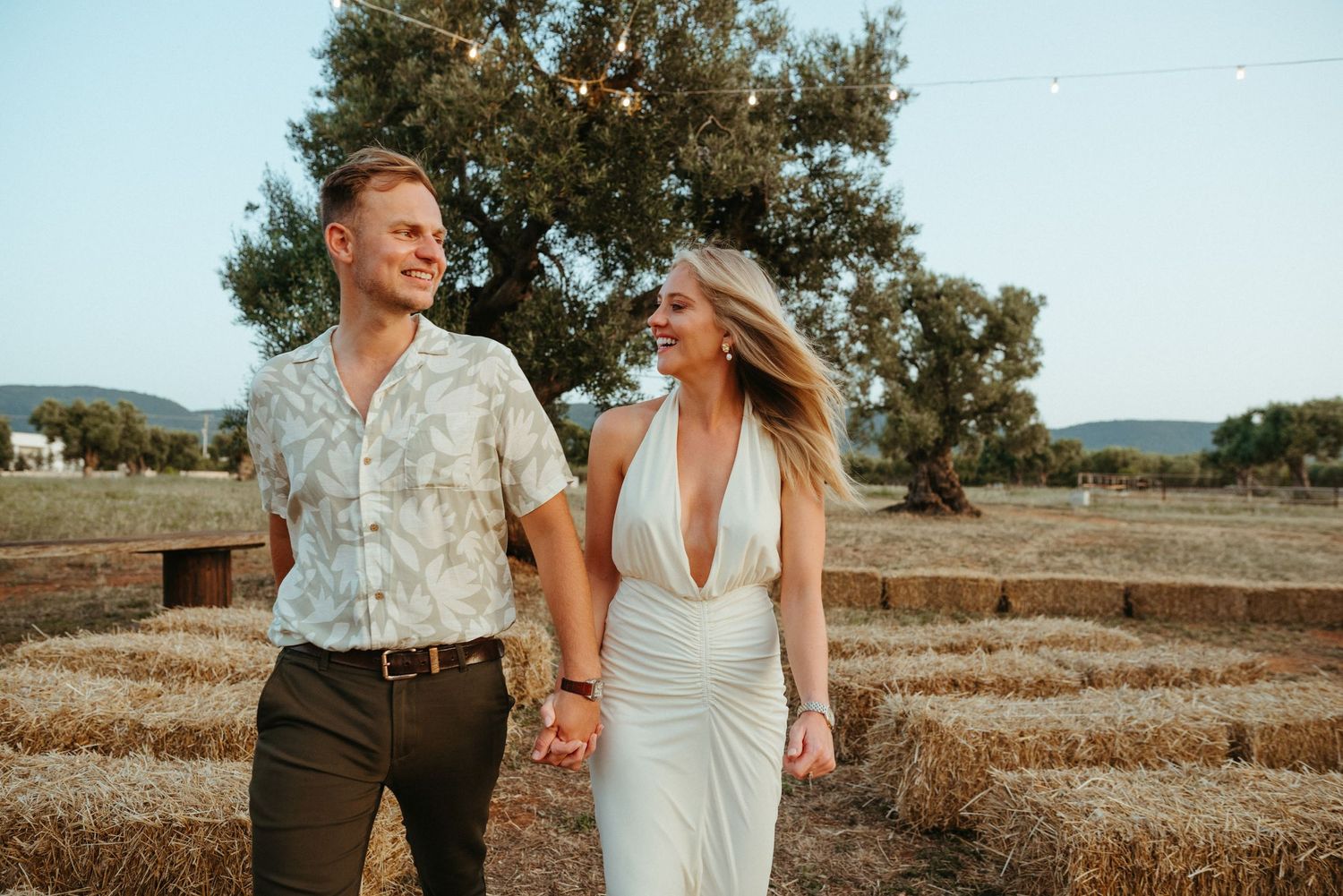 A couple shares a tender moment in a sun-drenched field with stone walls in the background.